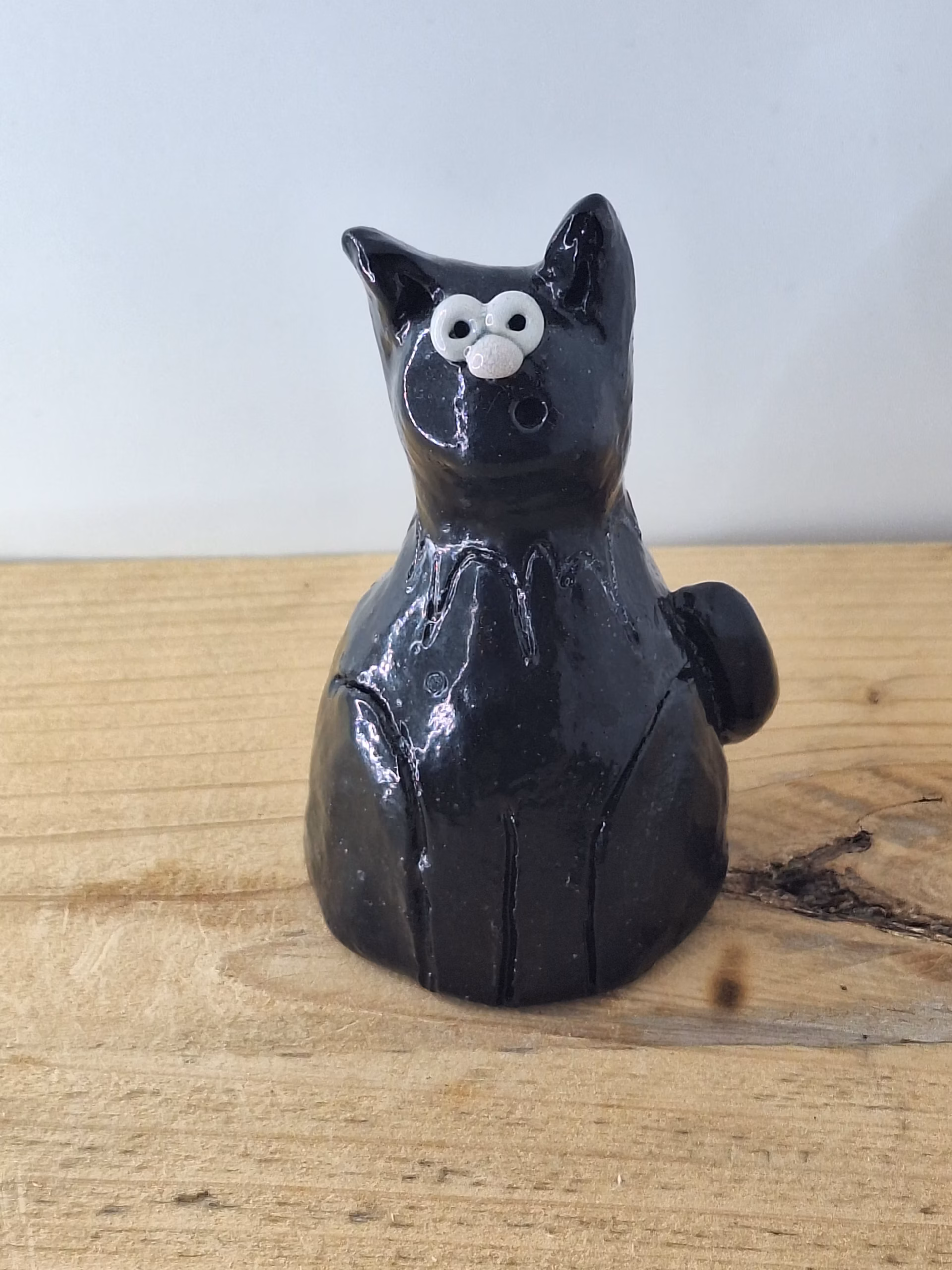 Small black ceramic cat with wide white eyes and pointed ears, sitting upright with a contemplative expression.