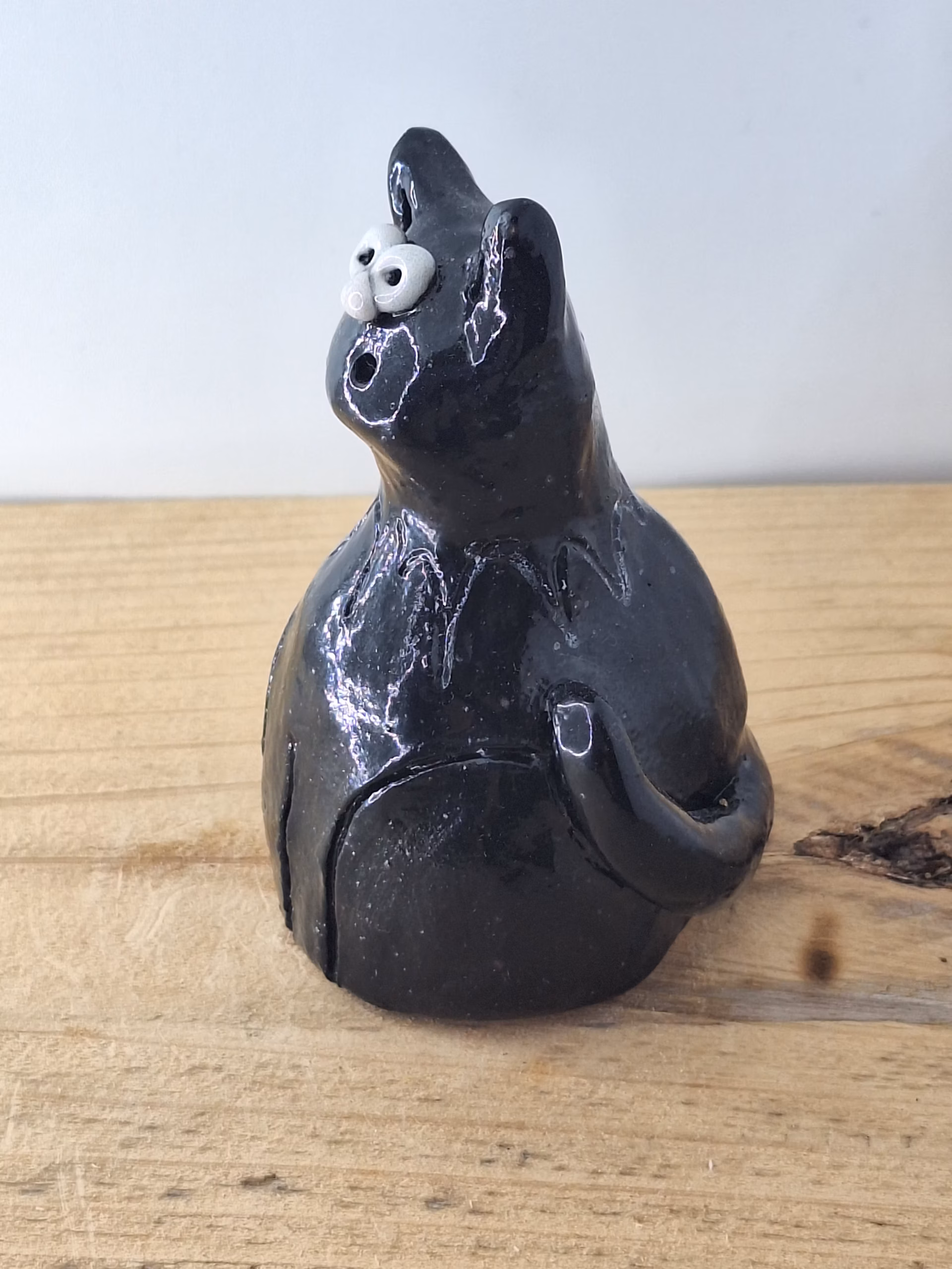 Small black ceramic cat with wide white eyes and pointed ears, sitting upright with a contemplative expression.