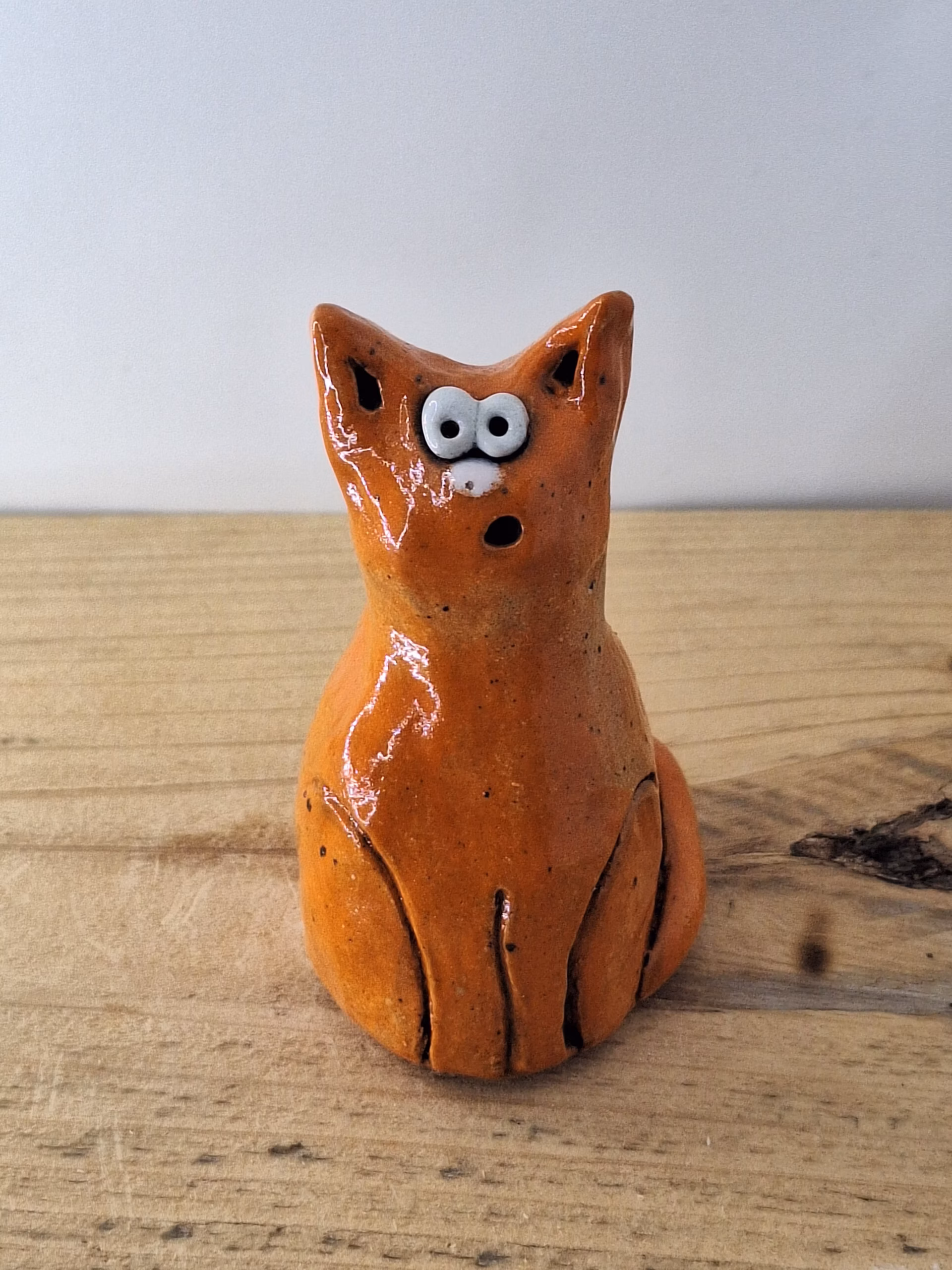 small ceramic cat figurine with pointed ears, wide surprised eyes, and terracotta glaze with dark markings.