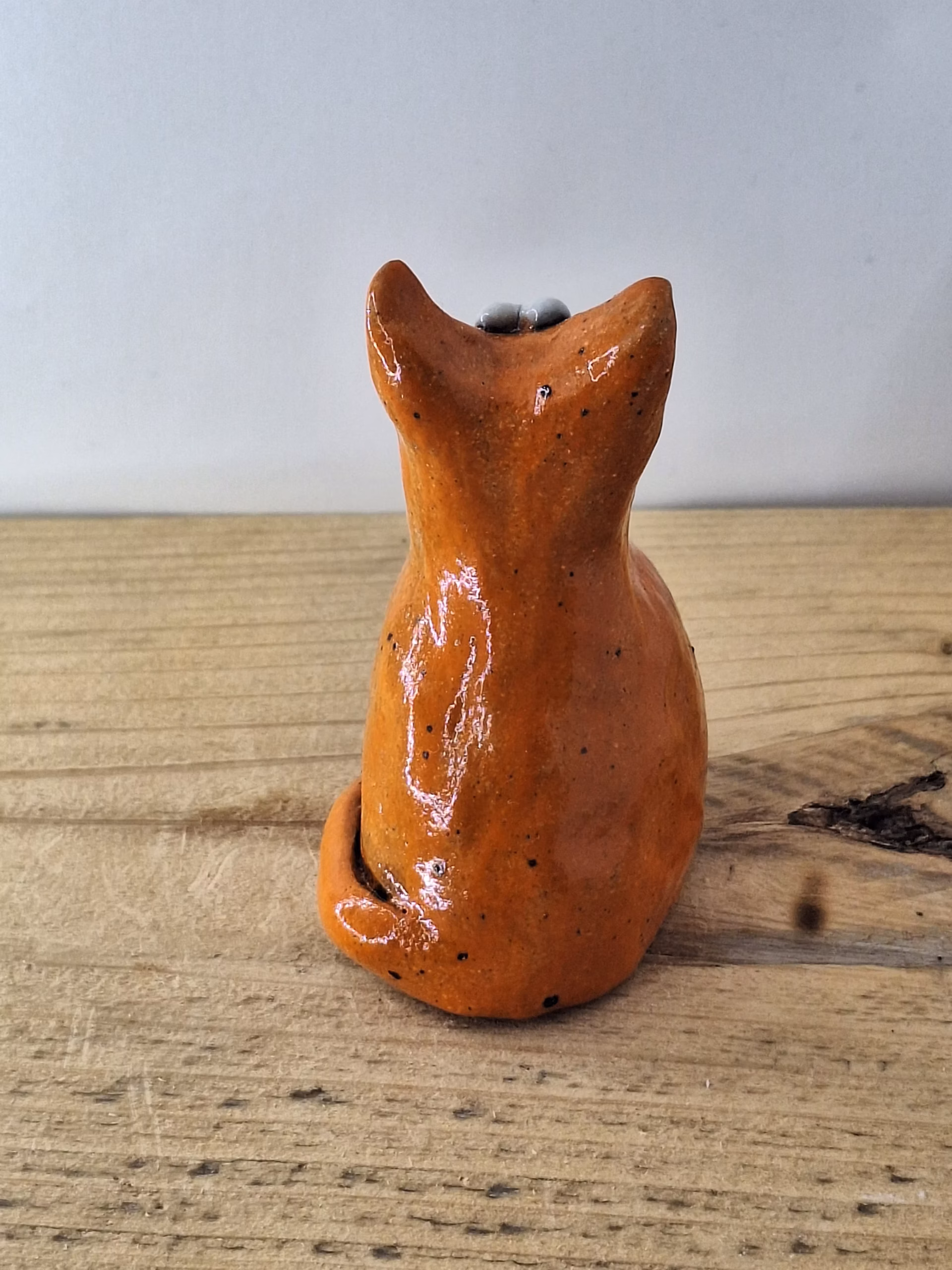 small ceramic cat figurine with pointed ears, wide surprised eyes, and terracotta glaze with dark markings.