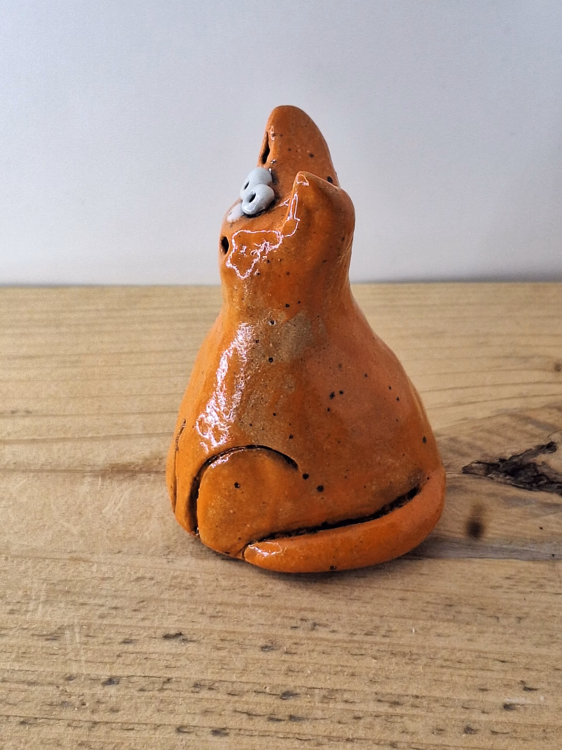 small ceramic cat figurine with pointed ears, wide surprised eyes, and terracotta glaze with dark markings.