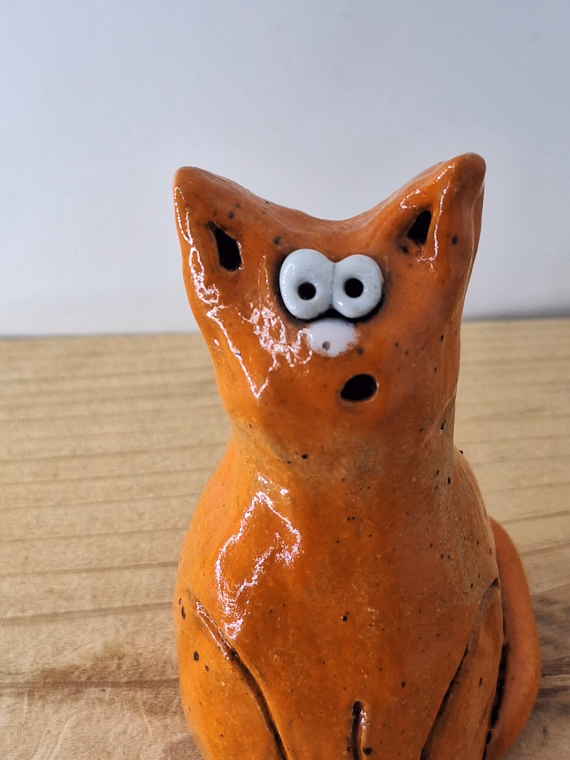 small ceramic cat figurine with pointed ears, wide surprised eyes, and terracotta glaze with dark markings.