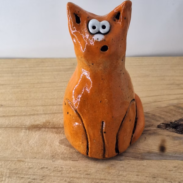 small ceramic cat figurine with pointed ears, wide surprised eyes, and terracotta glaze with dark markings.