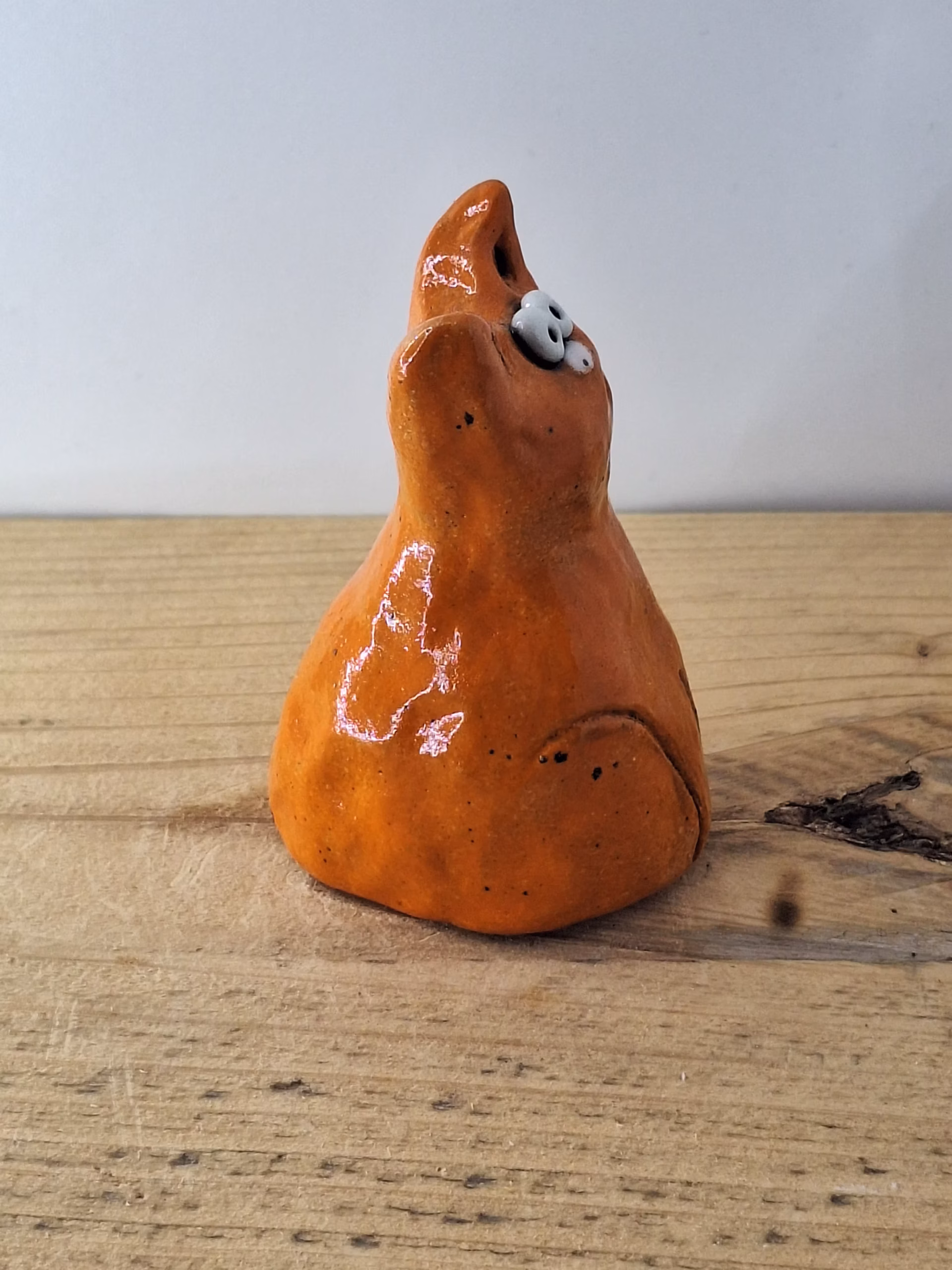 small ceramic cat figurine with pointed ears, wide surprised eyes, and terracotta glaze with dark markings.