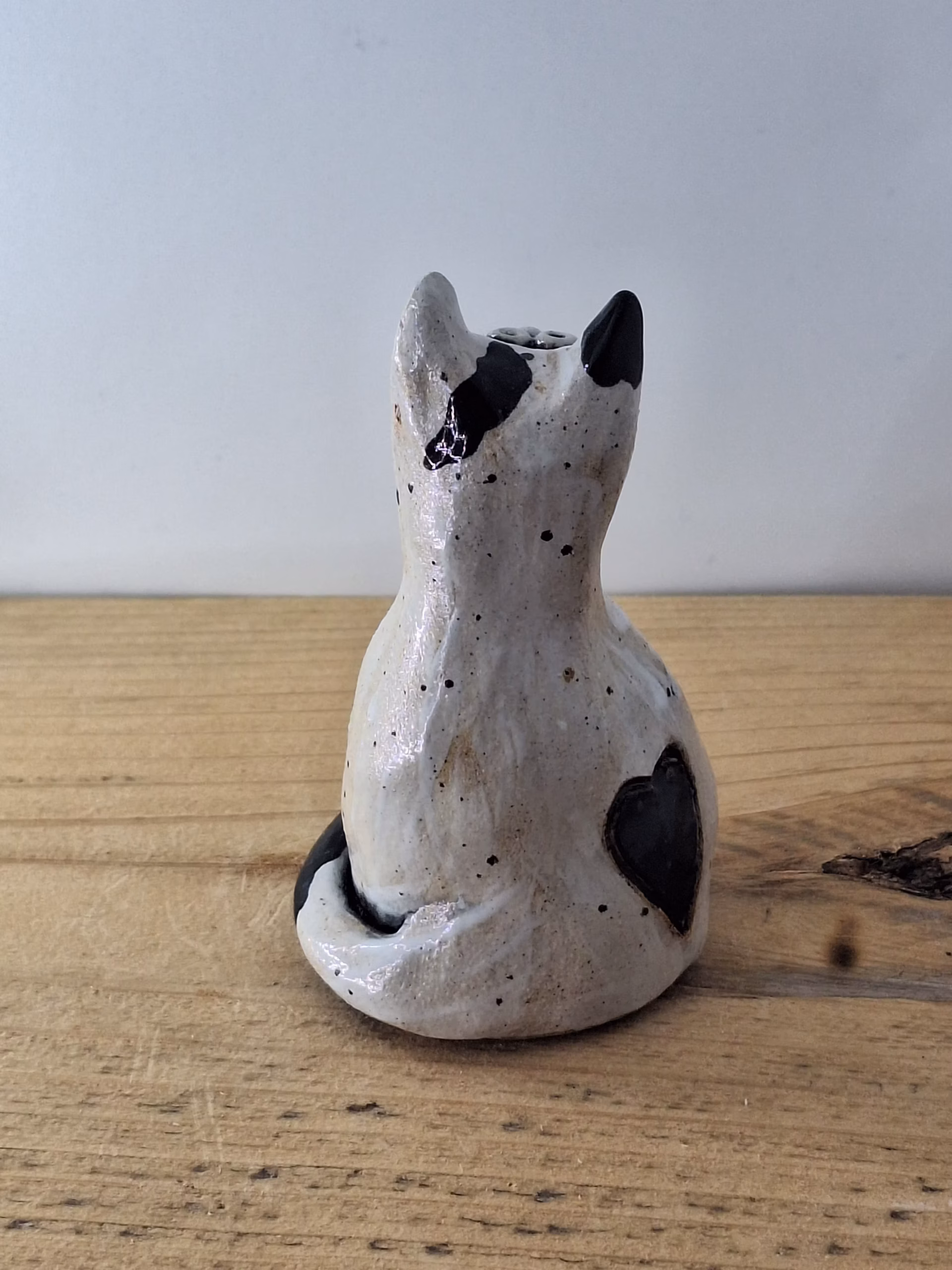Small ceramic cat figurine with white glaze, black painted details, wide eyes and pink nose, sitting upright.