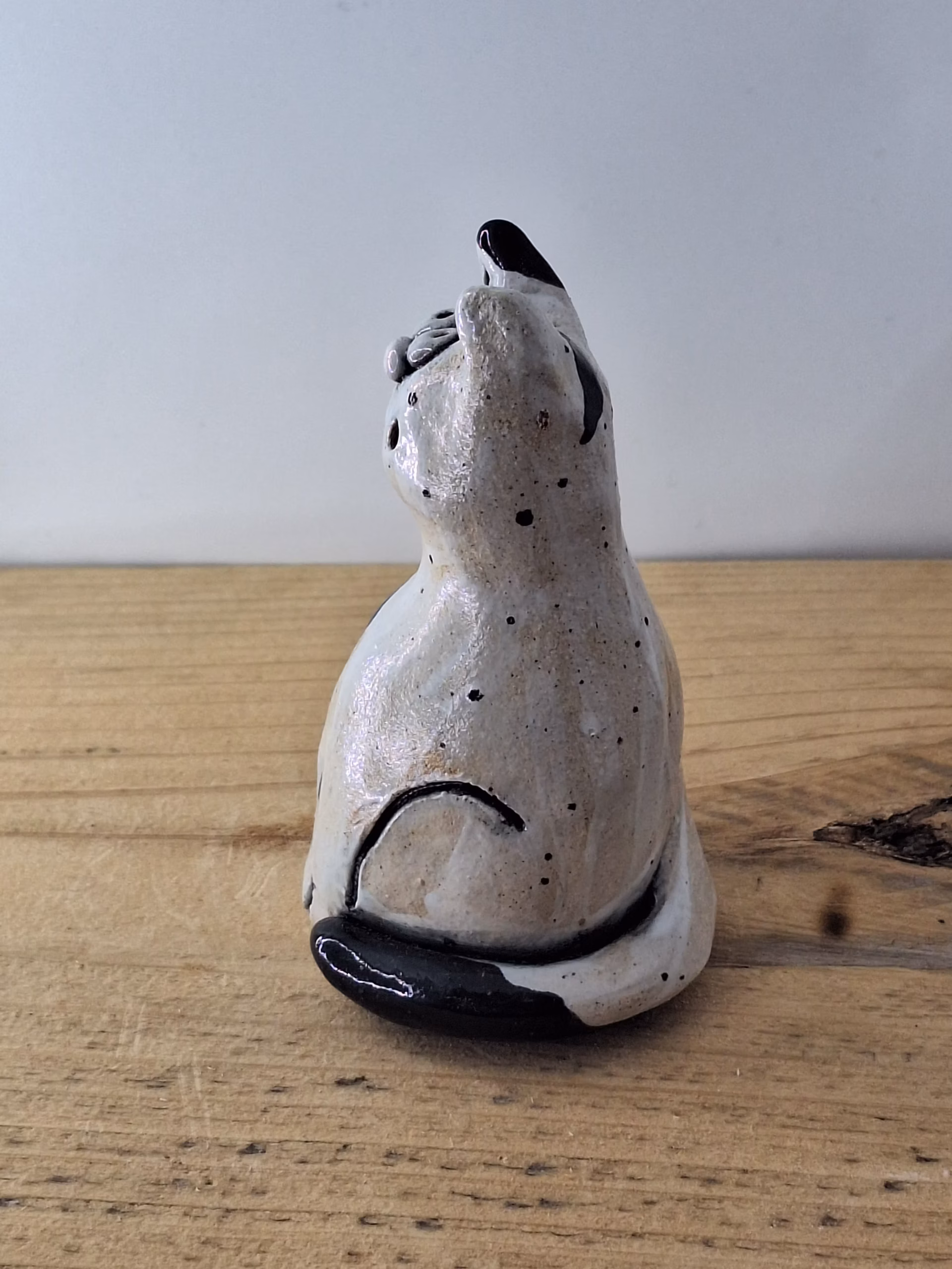 Small ceramic cat figurine with white glaze, black painted details, wide eyes and pink nose, sitting upright.