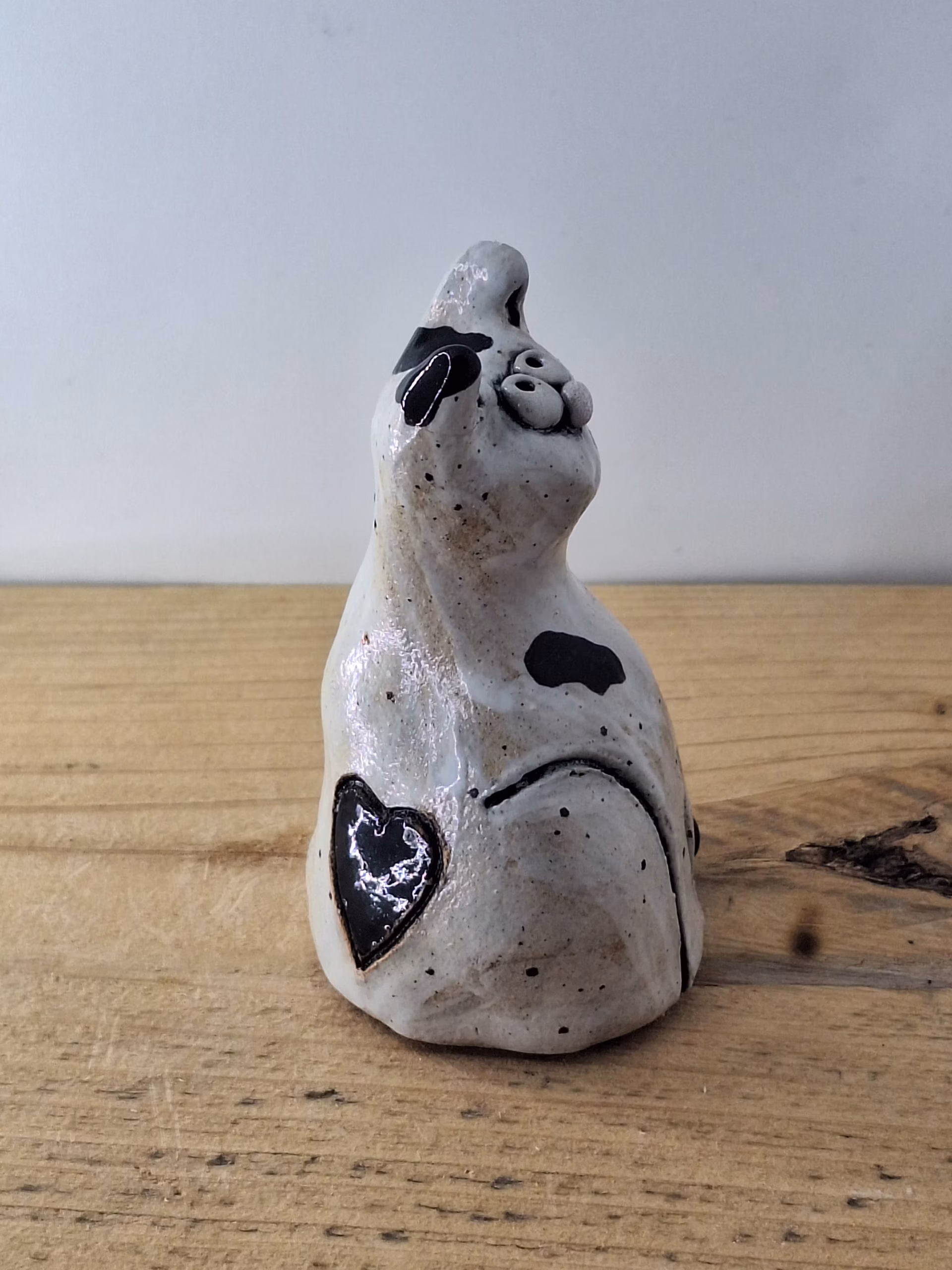 Small ceramic cat figurine with white glaze, black painted details, wide eyes and pink nose, sitting upright.