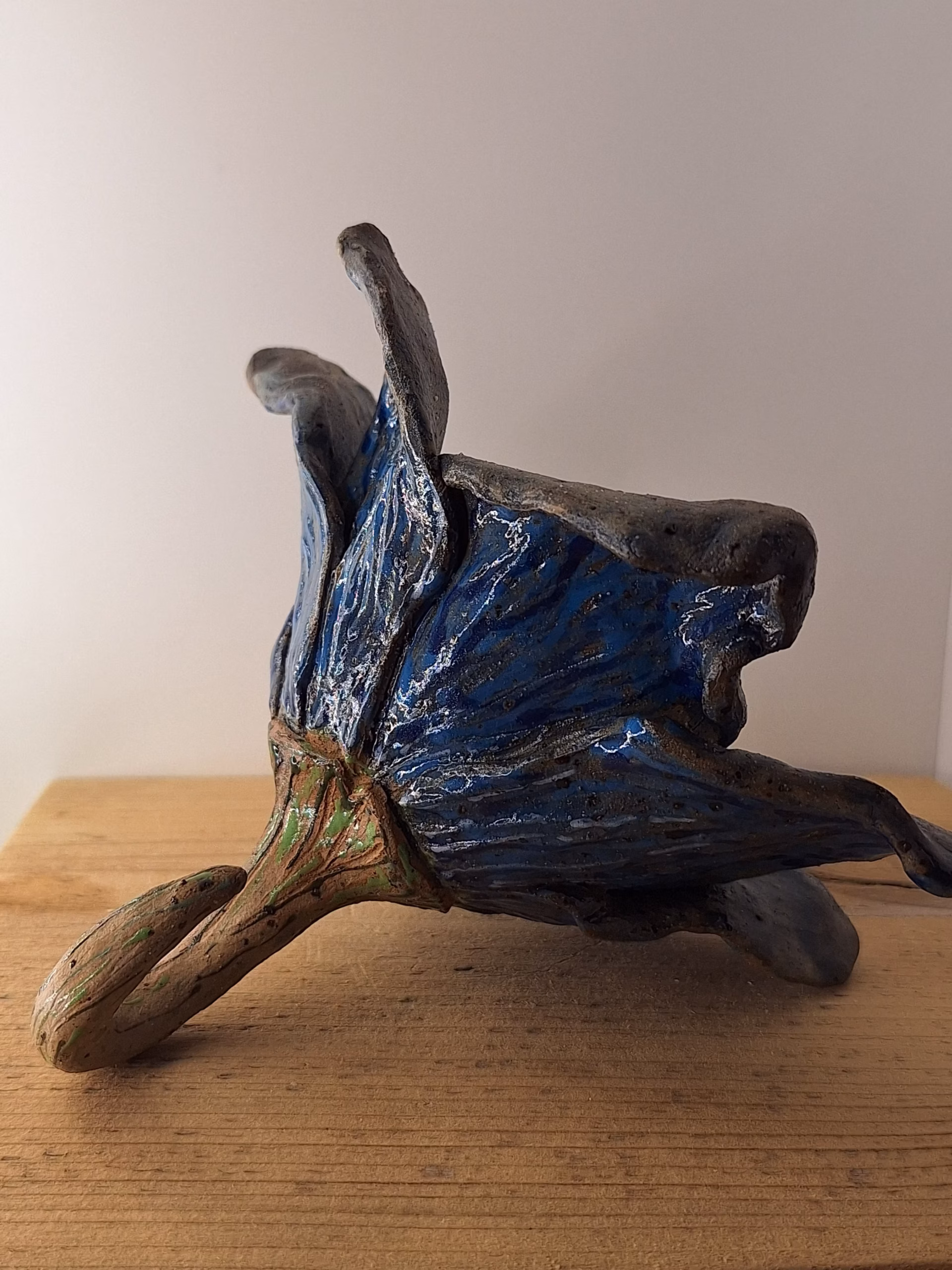 Small ceramic fairy house shaped like a bulbous acorn with deep wood-grain texture, deep blue draped fabric, curved hook stem, and a small heart-shaped door.