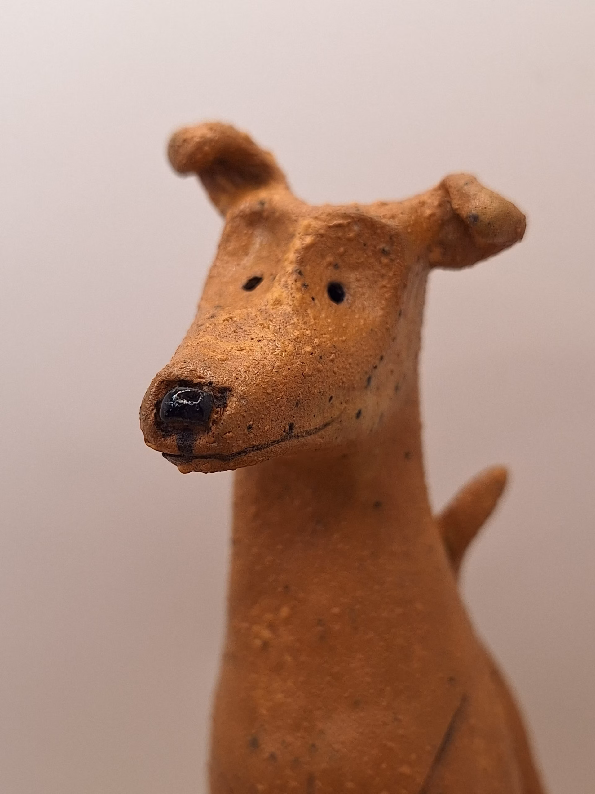Small ceramic dog figurine with pointed ears, black nose and eyes, textured terracotta surface.