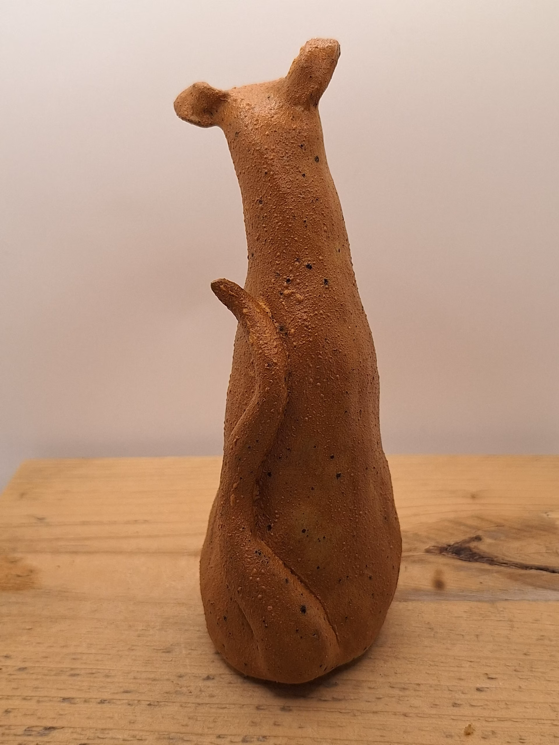 Small ceramic dog figurine with pointed ears, black nose and eyes, textured terracotta surface.