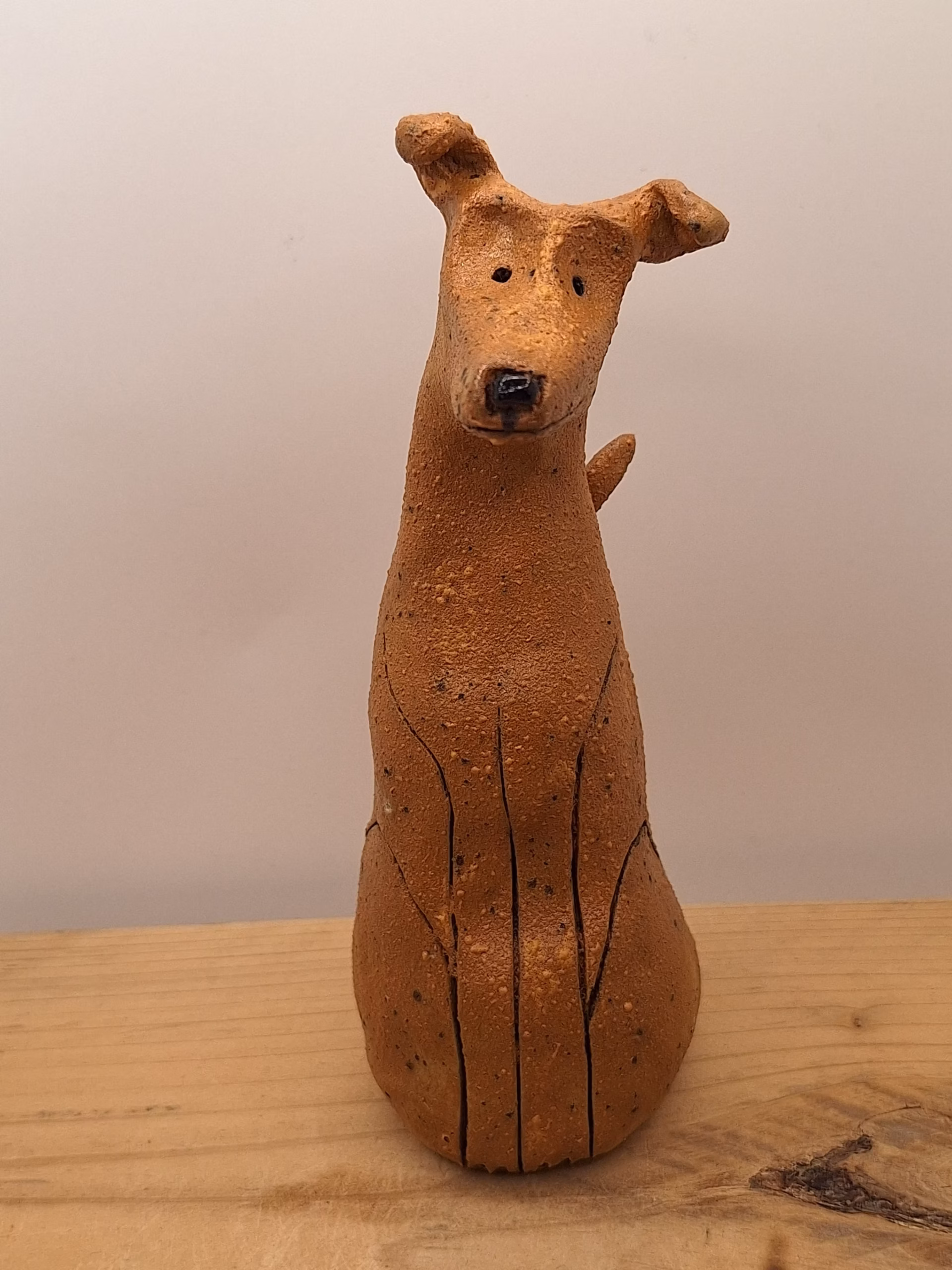 Small ceramic dog figurine with pointed ears, black nose and eyes, textured terracotta surface.