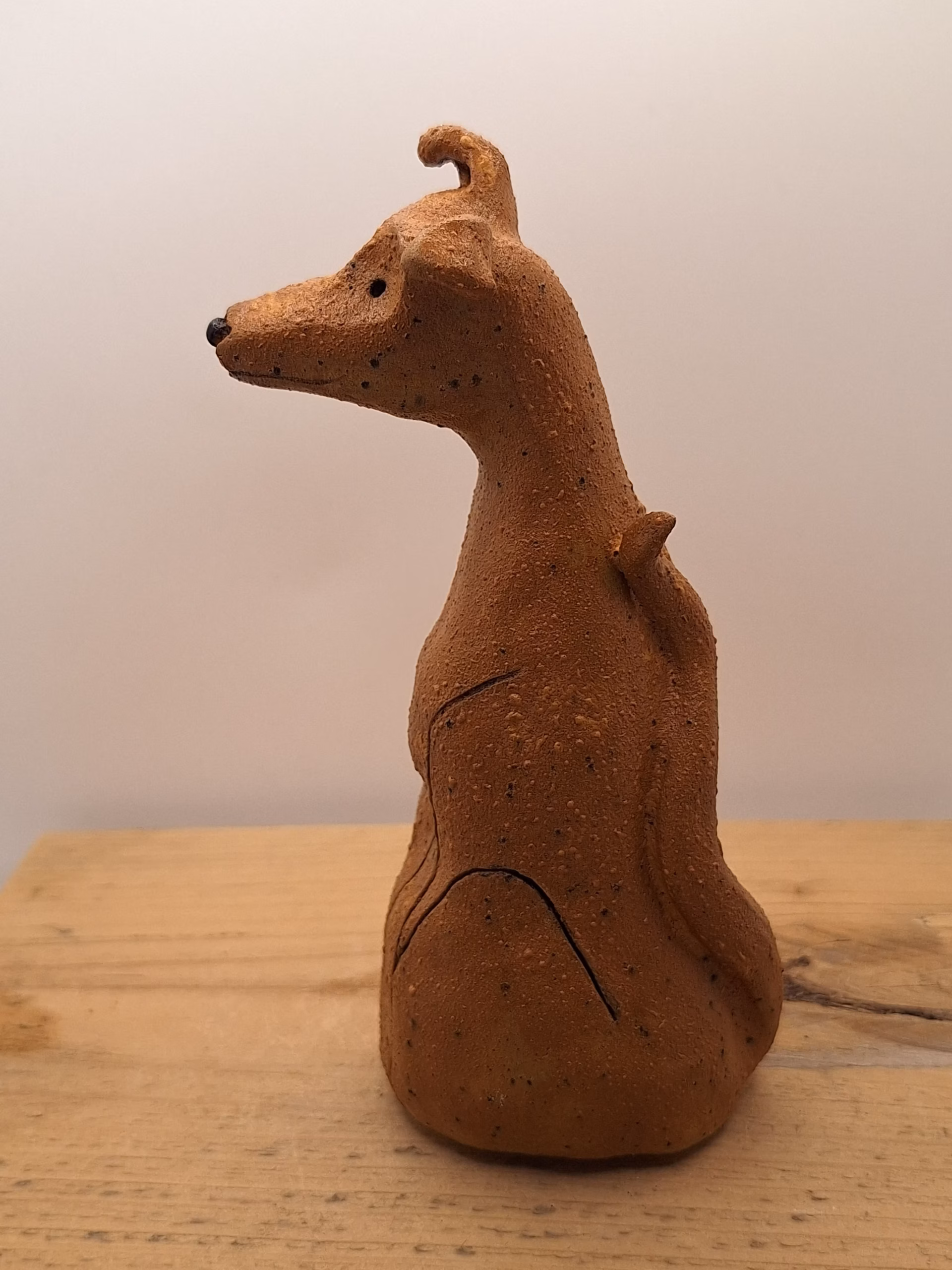 Small ceramic dog figurine with pointed ears, black nose and eyes, textured terracotta surface.