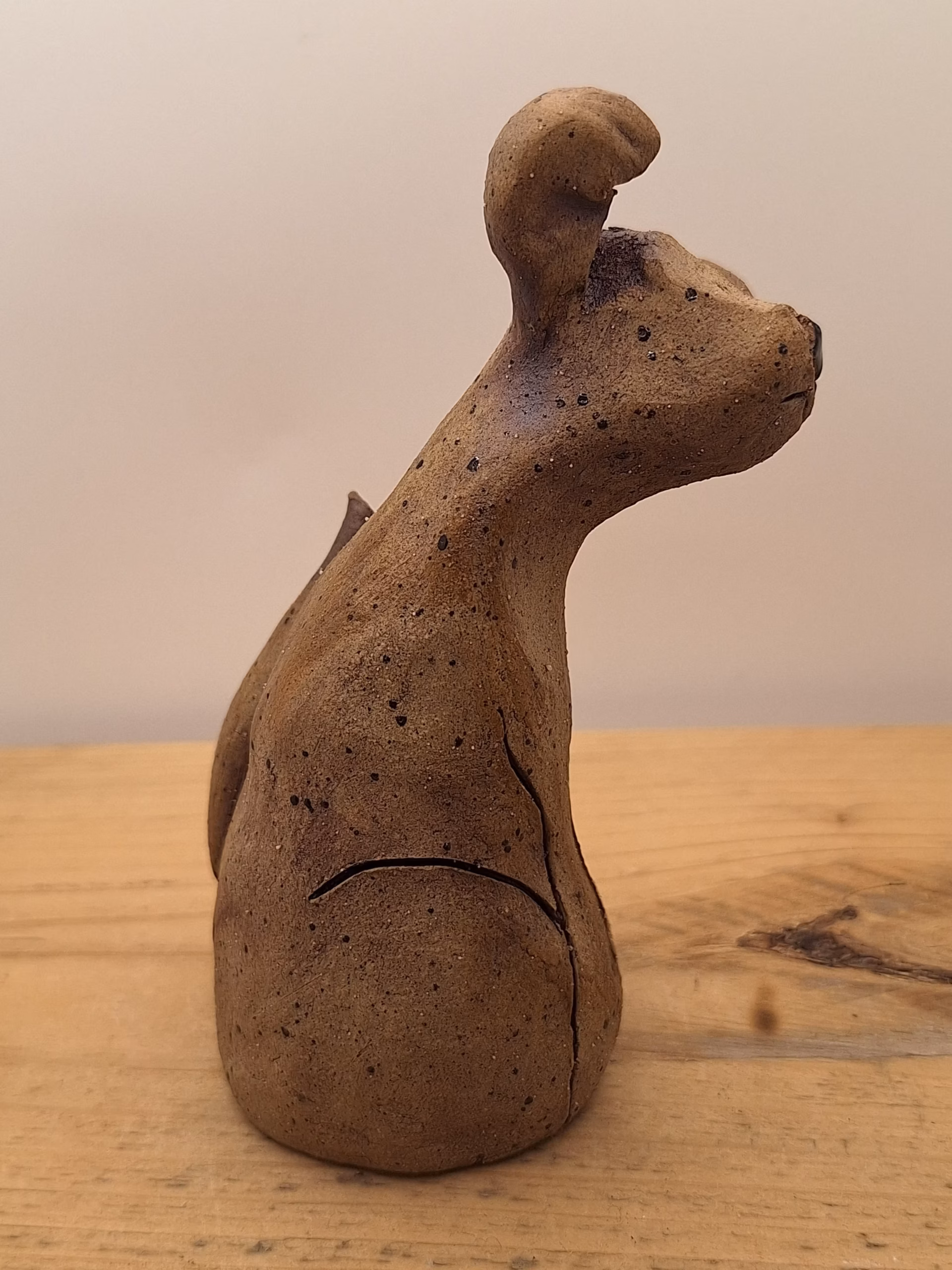 Small ceramic puppy with tilted head, black painted nose and eyes, textured surface, sitting upright.