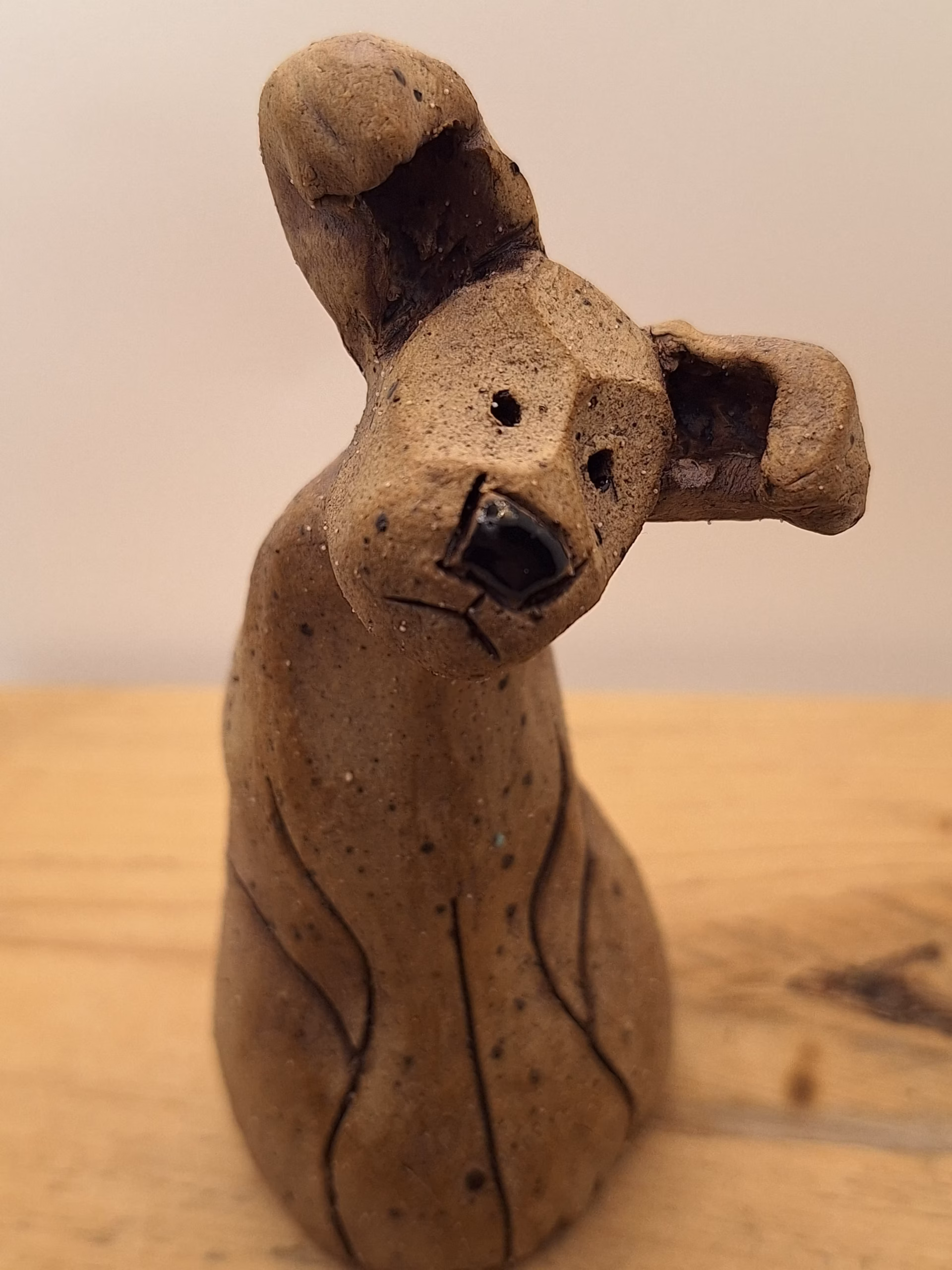 Small ceramic puppy with tilted head, black painted nose and eyes, textured surface, sitting upright.