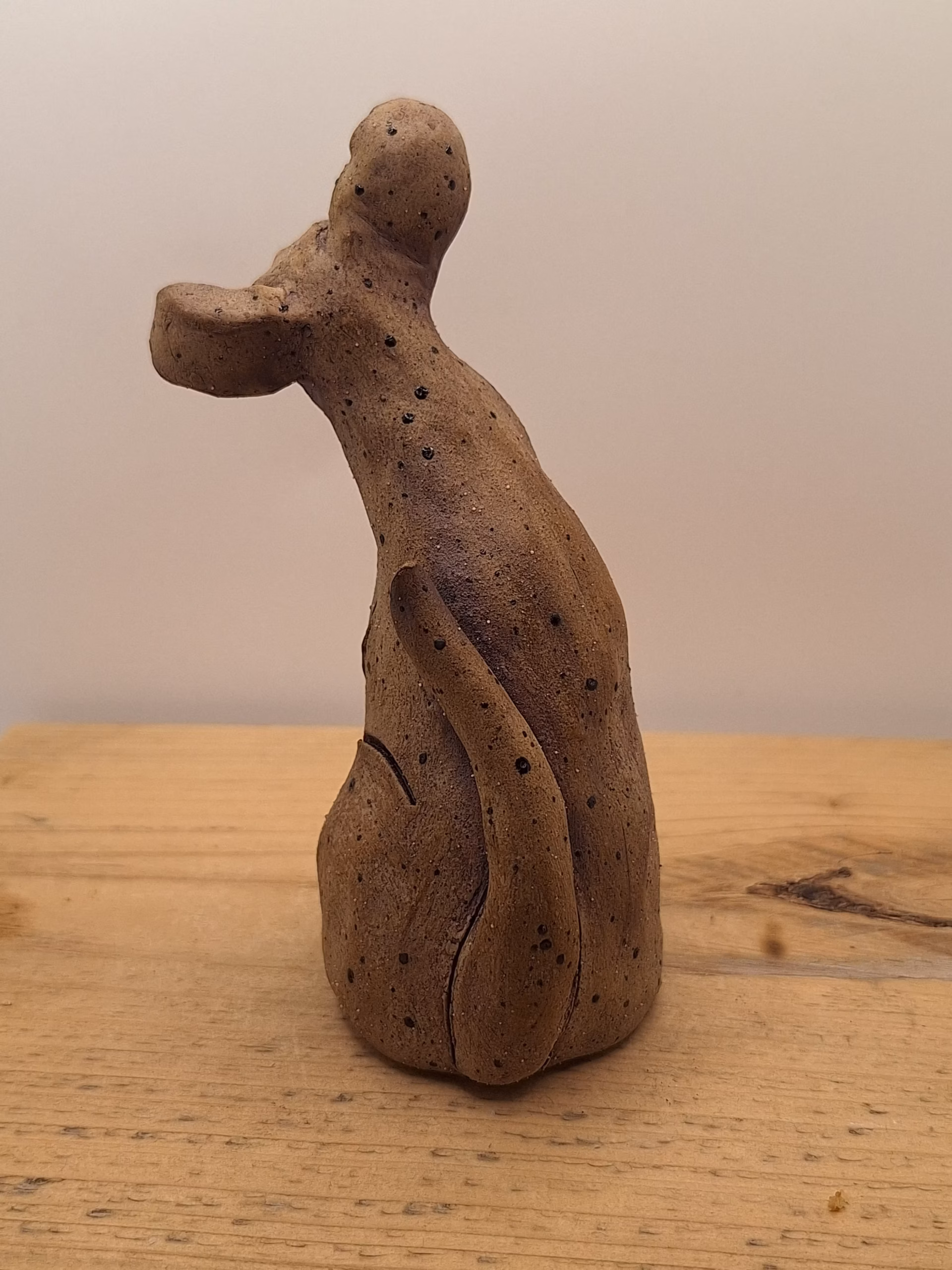 Small ceramic puppy with tilted head, black painted nose and eyes, textured surface, sitting upright.