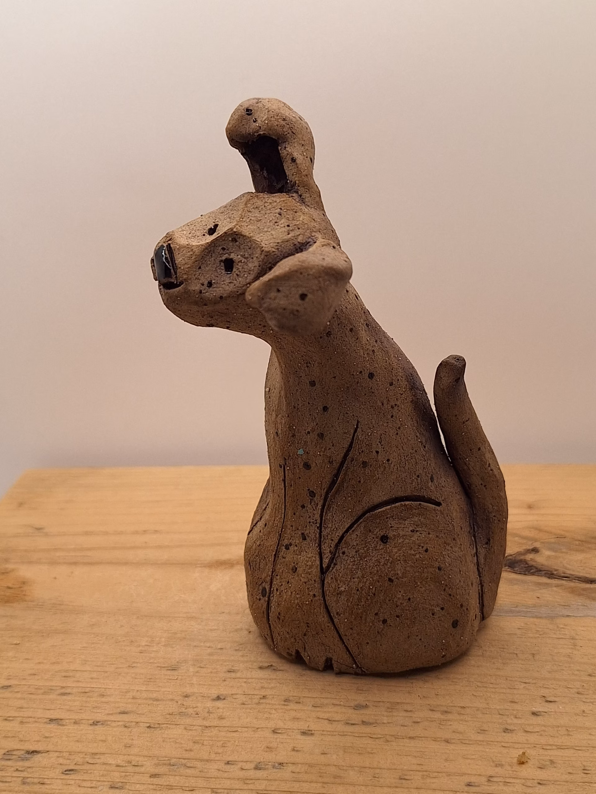 Small ceramic puppy with tilted head, black painted nose and eyes, textured surface, sitting upright.