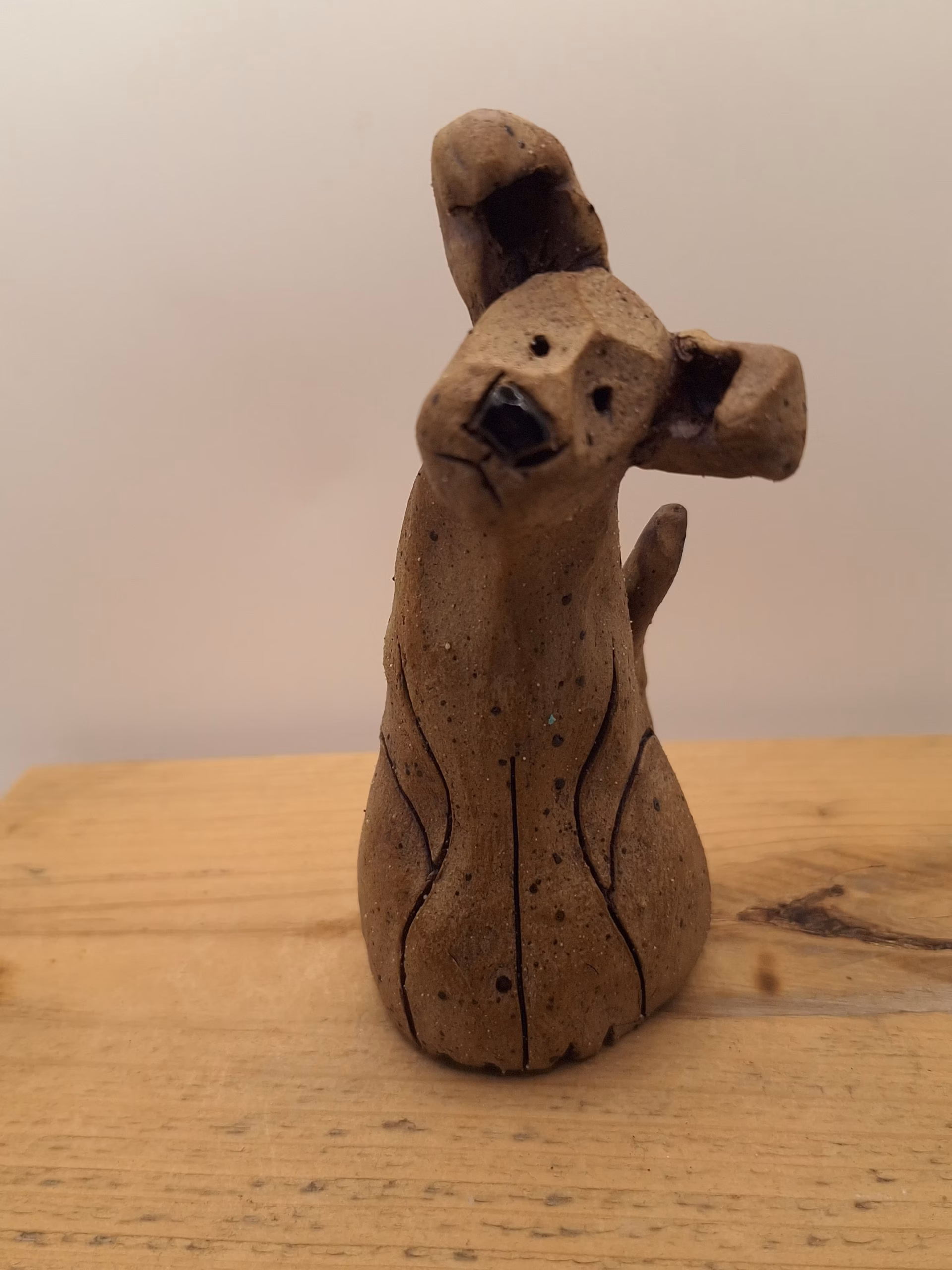 Small ceramic puppy with tilted head, black painted nose and eyes, textured surface, sitting upright.