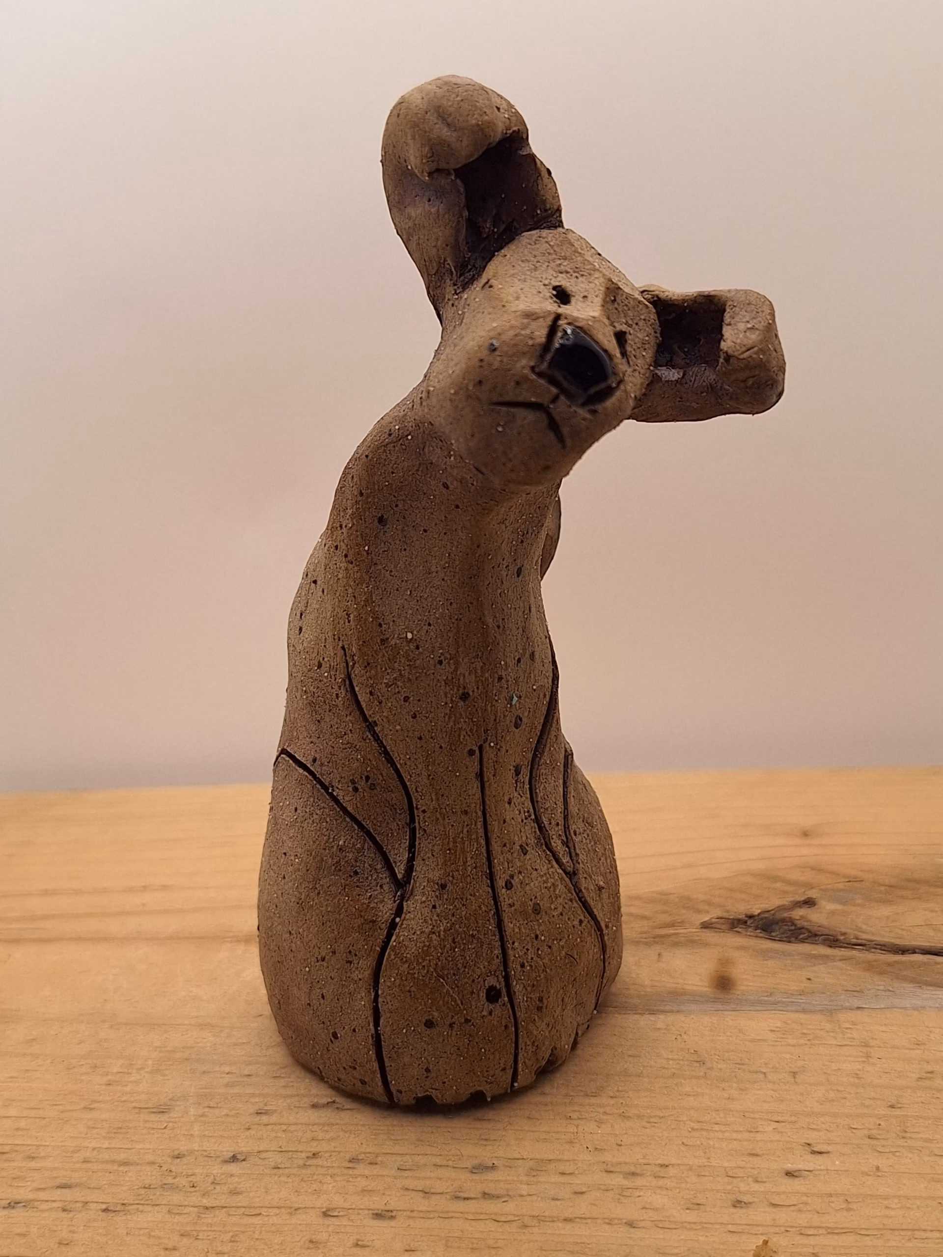 Small ceramic puppy with tilted head, black painted nose and eyes, textured surface, sitting upright.