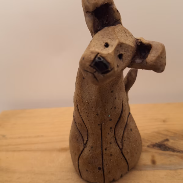 Small ceramic puppy with tilted head, black painted nose and eyes, textured surface, sitting upright.