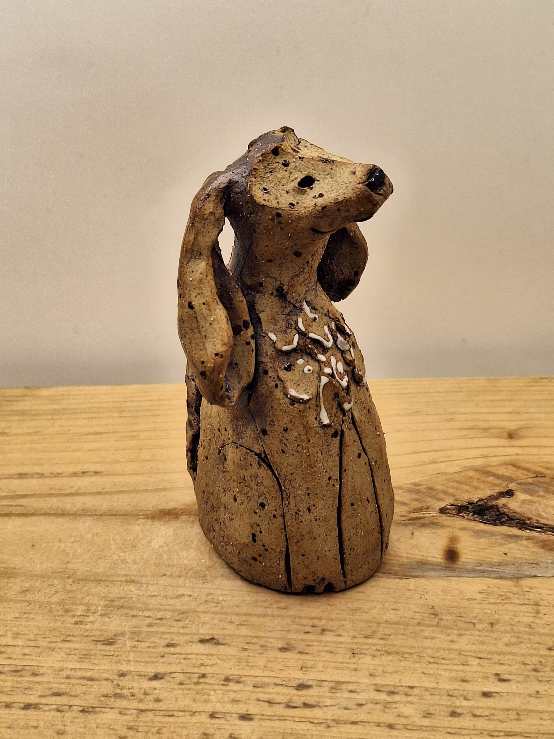 Small ceramic dog figurine with long ears, speckled brown glaze, and white painted markings on chest.