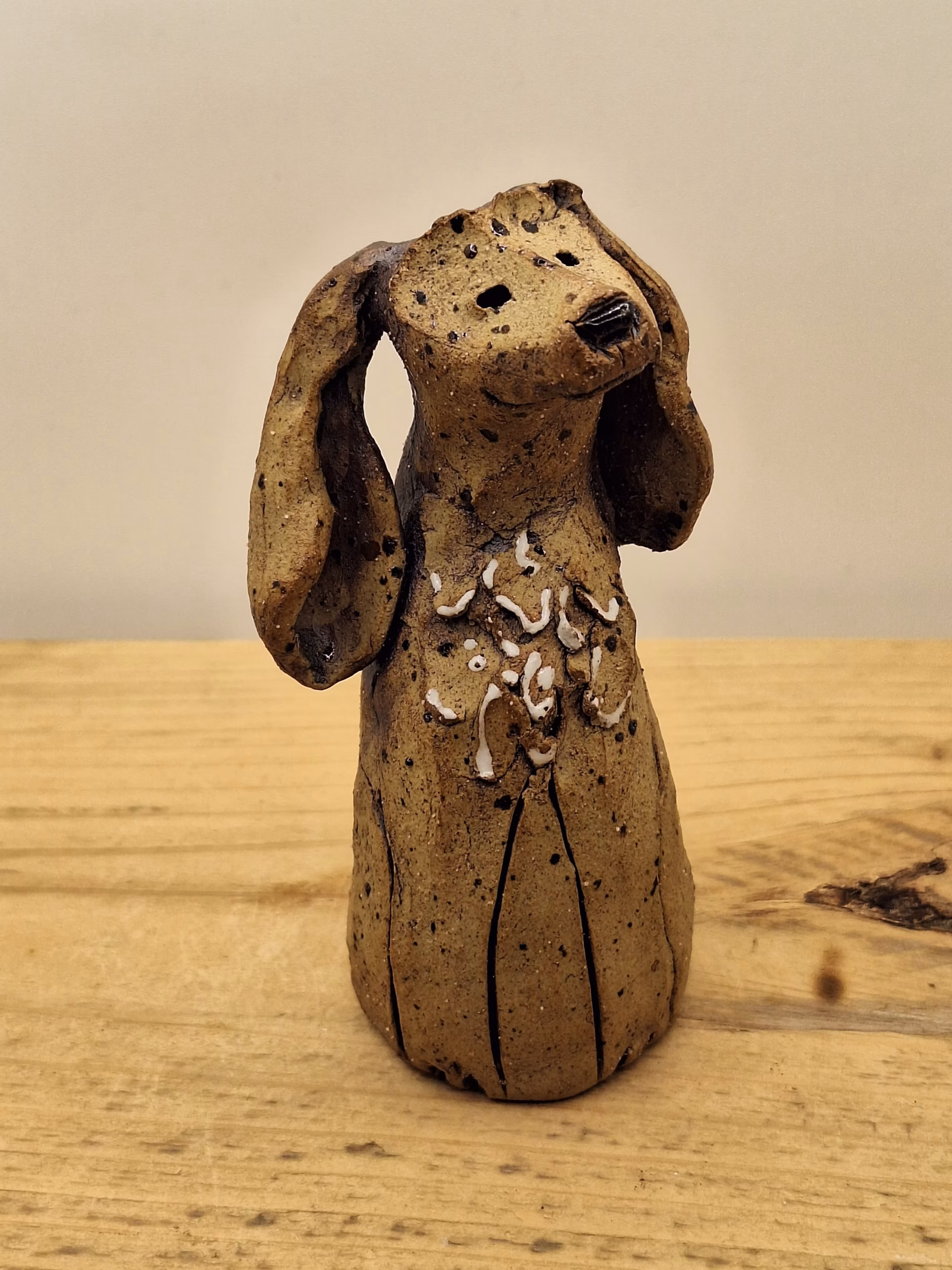 Small ceramic dog figurine with long ears, speckled brown glaze, and white painted markings on chest.
