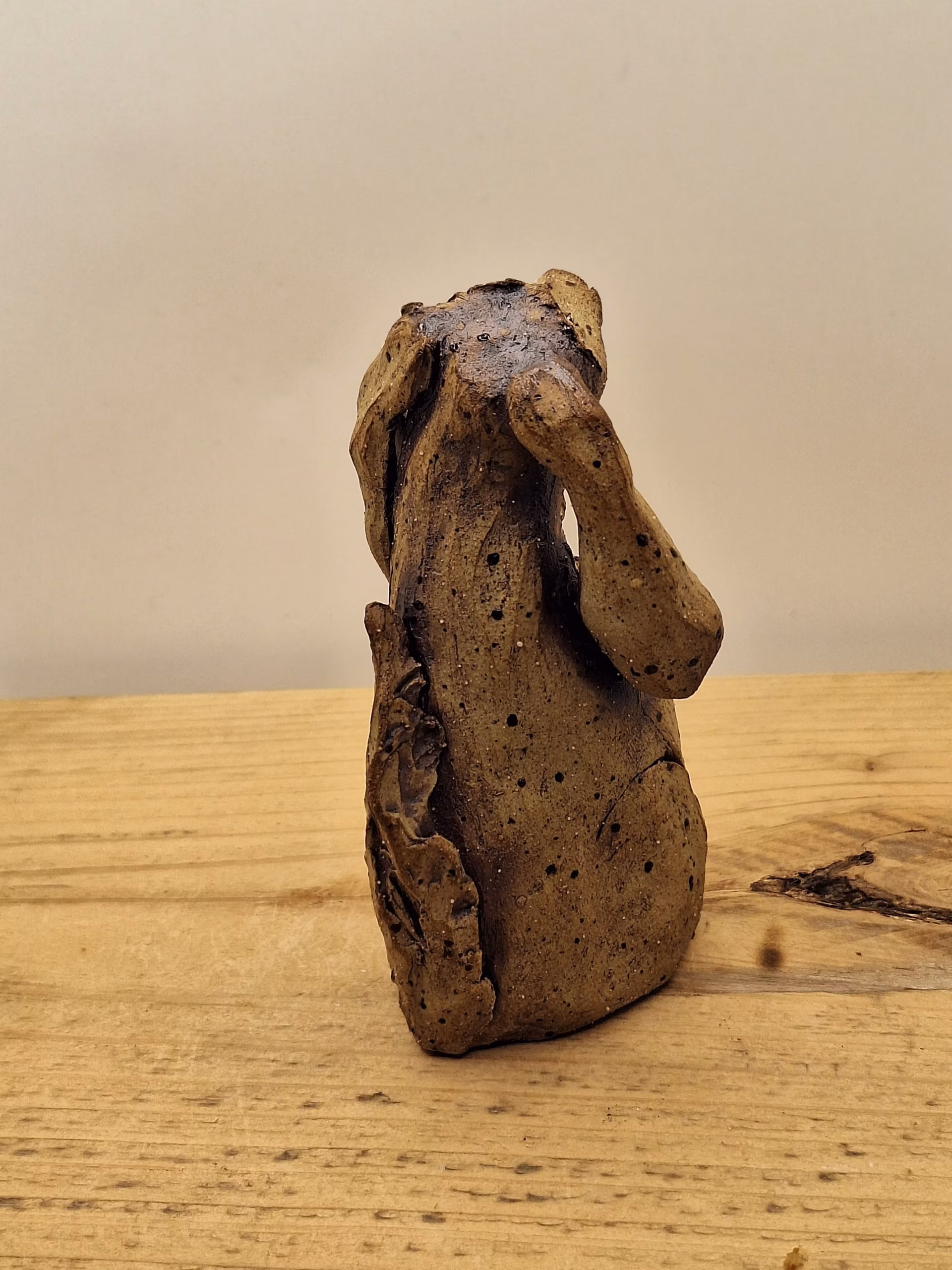 Small ceramic dog figurine with long ears, speckled brown glaze, and white painted markings on chest.