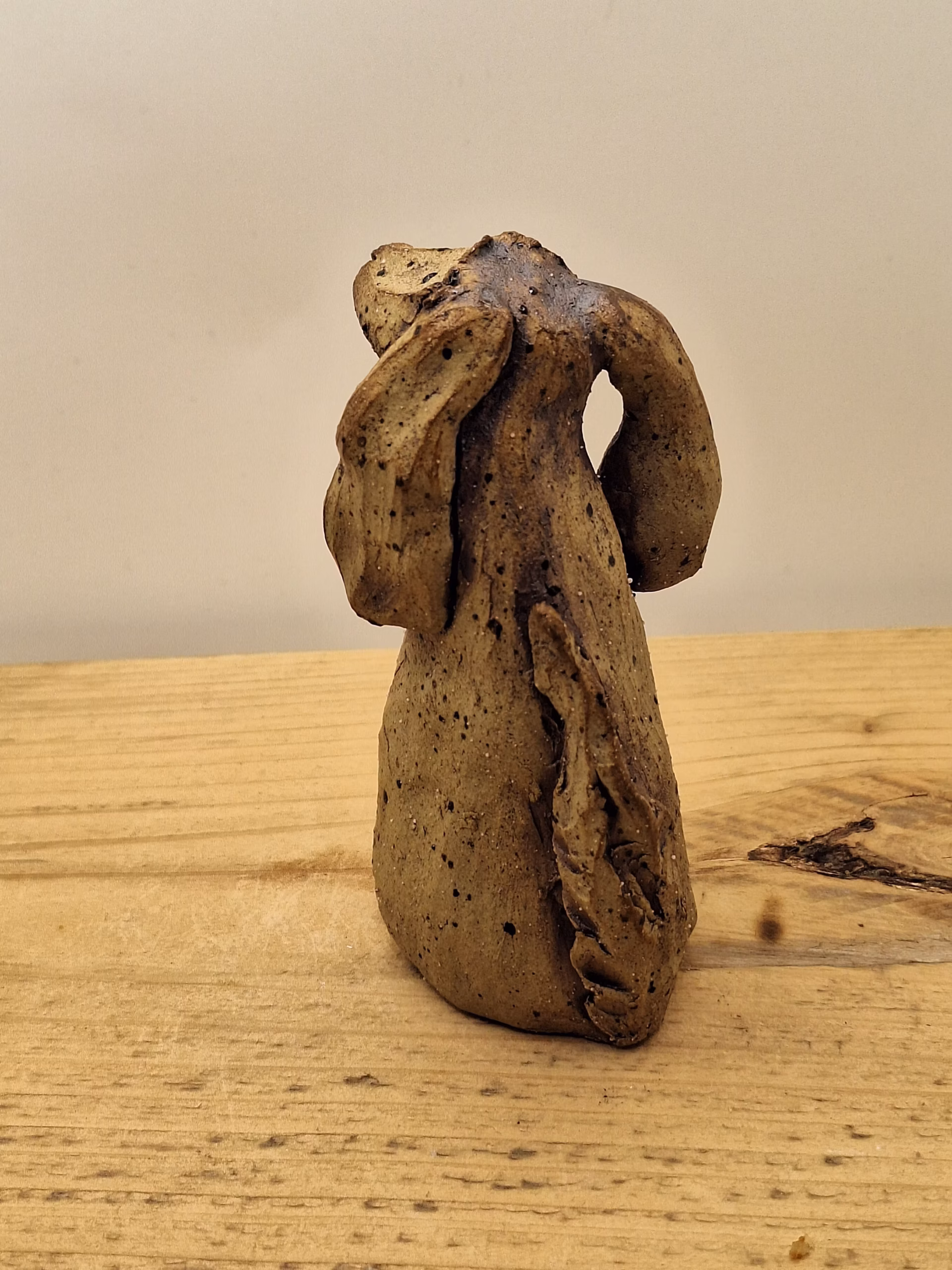 Small ceramic dog figurine with long ears, speckled brown glaze, and white painted markings on chest.