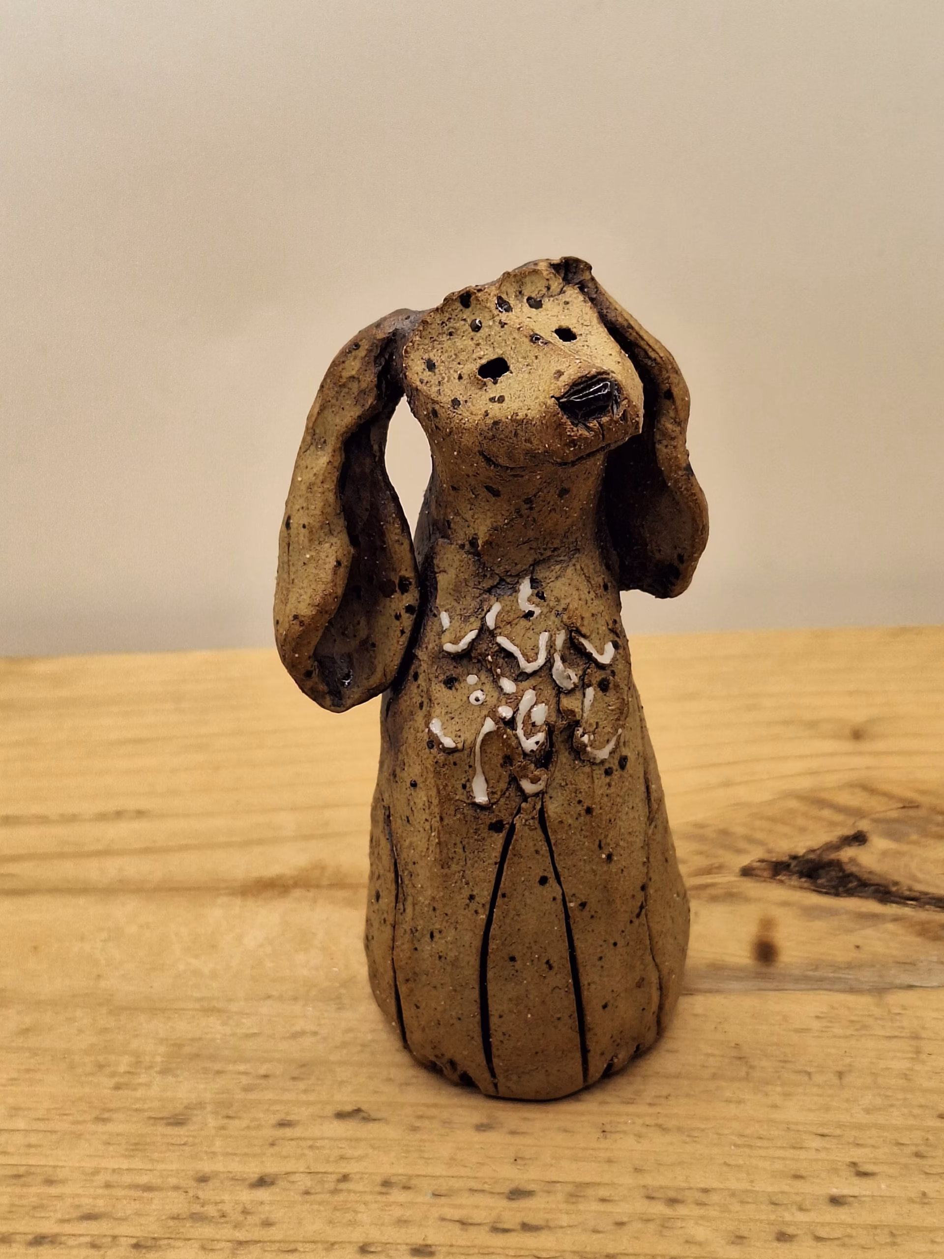 Small ceramic dog figurine with long ears, speckled brown glaze, and white painted markings on chest.