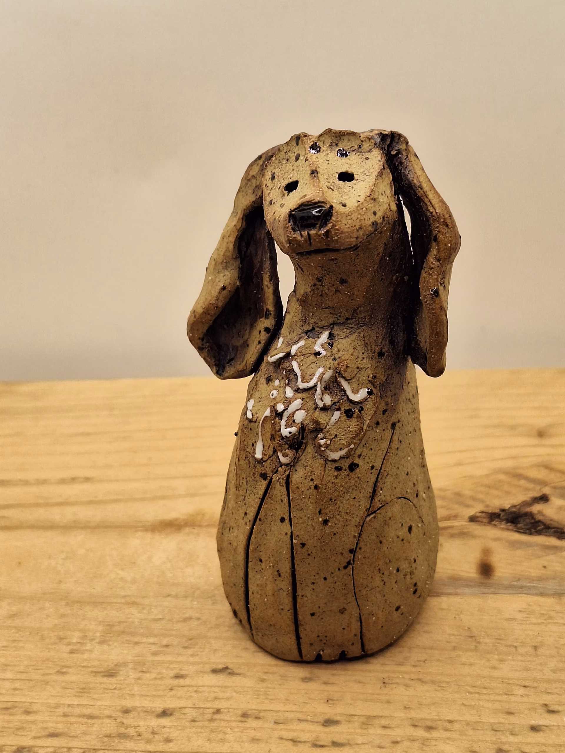 Small ceramic dog figurine with long ears, speckled brown glaze, and white painted markings on chest.