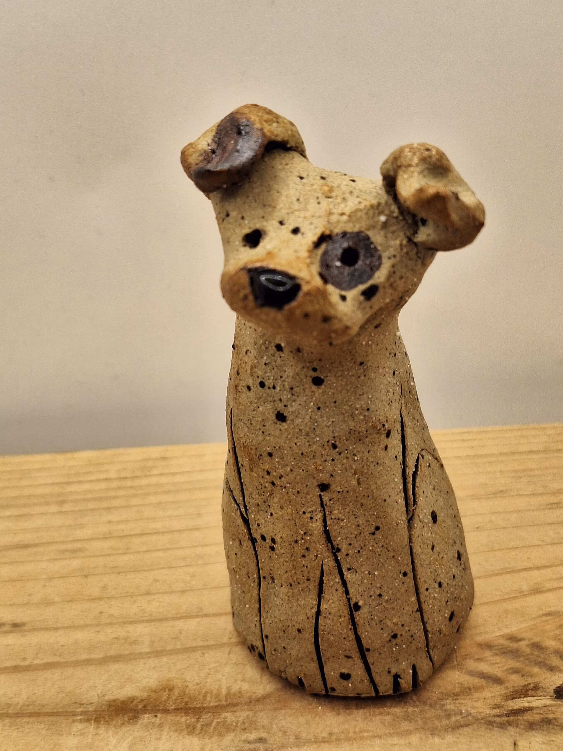 Small ceramic dog figurine with pointed ears, black painted eyes and mouth, speckled surface, sitting upright.