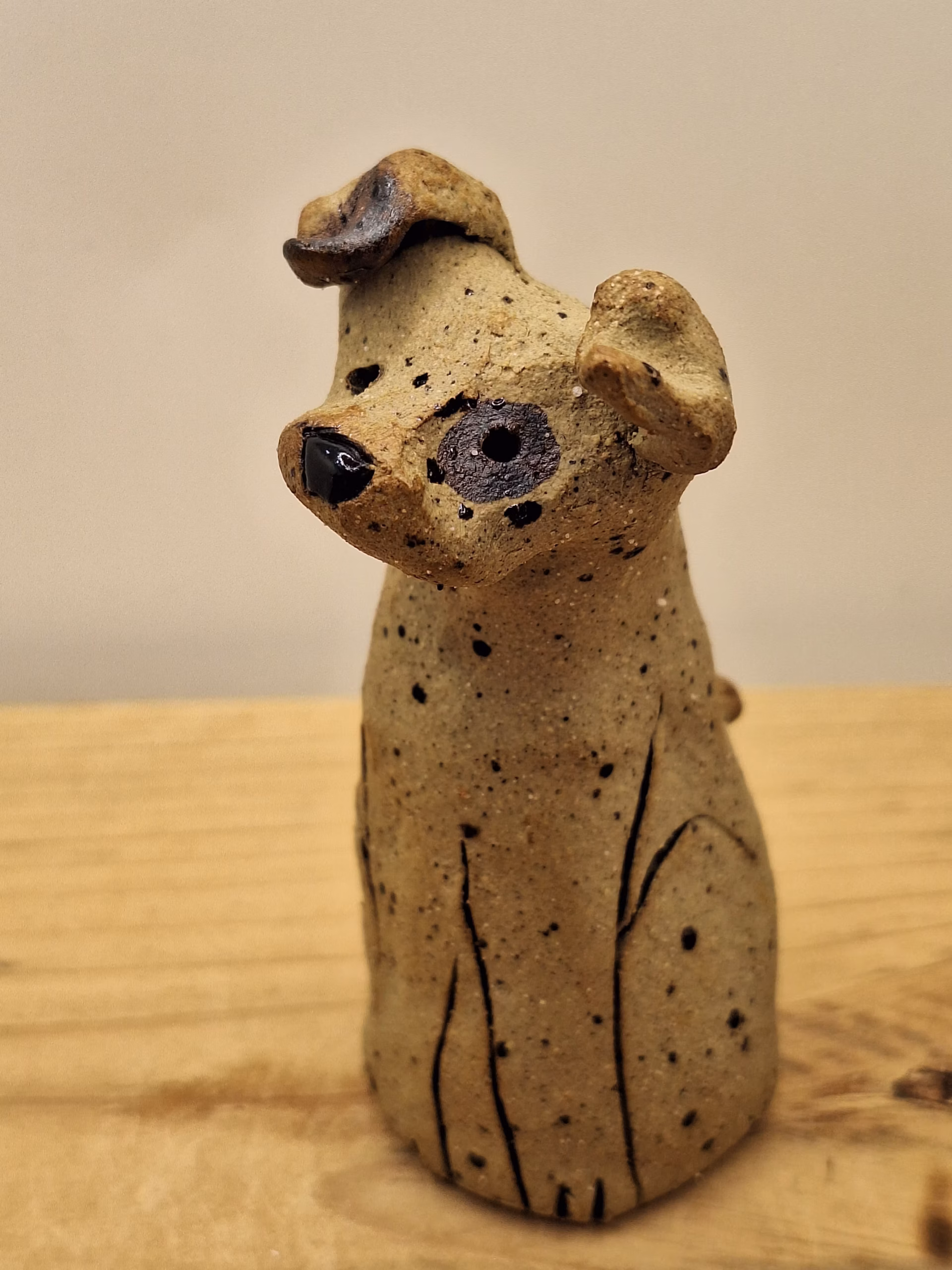 Small ceramic dog figurine with pointed ears, black painted eyes and mouth, speckled surface, sitting upright.
