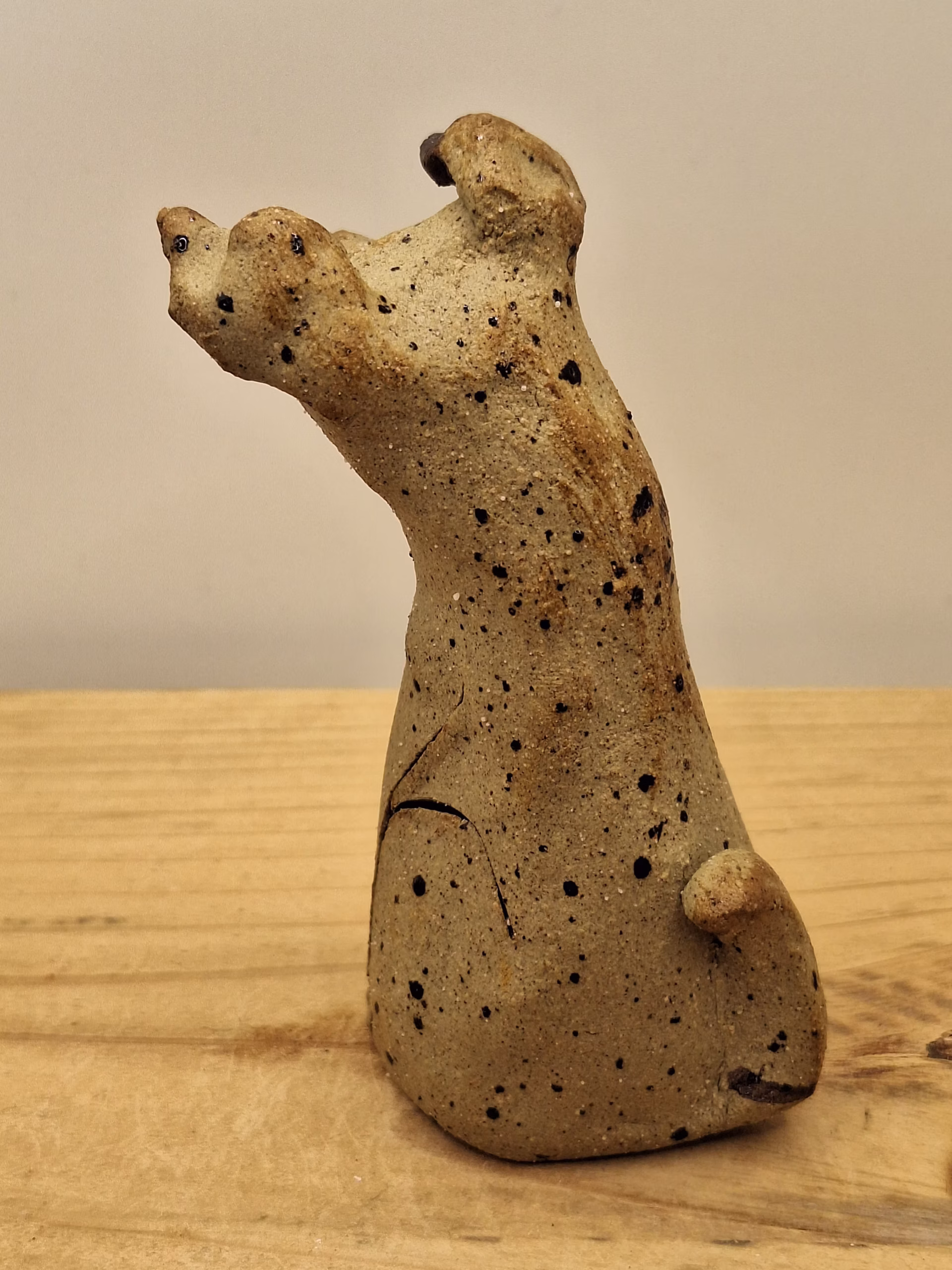 Small ceramic dog figurine with pointed ears, black painted eyes and mouth, speckled surface, sitting upright.