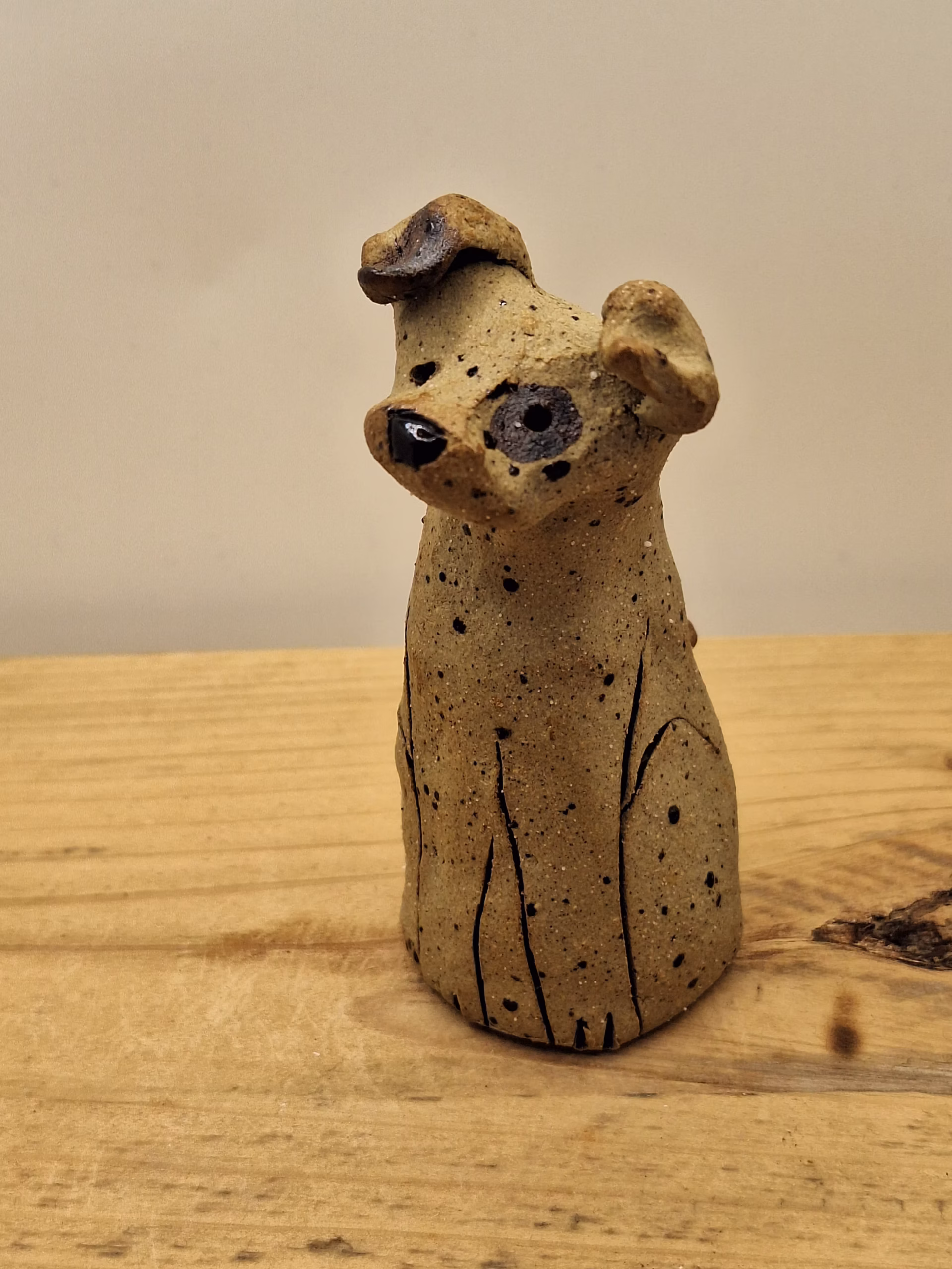 Small ceramic dog figurine with pointed ears, black painted eyes and mouth, speckled surface, sitting upright.