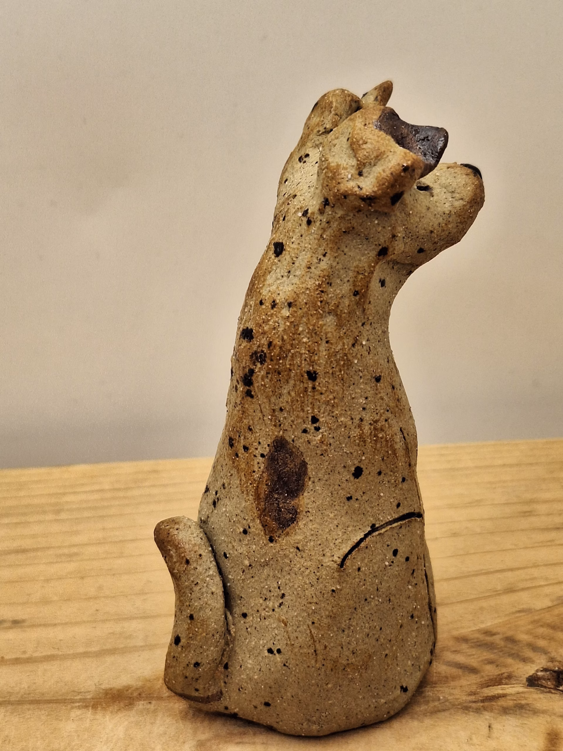 Small ceramic dog figurine with pointed ears, black painted eyes and mouth, speckled surface, sitting upright.