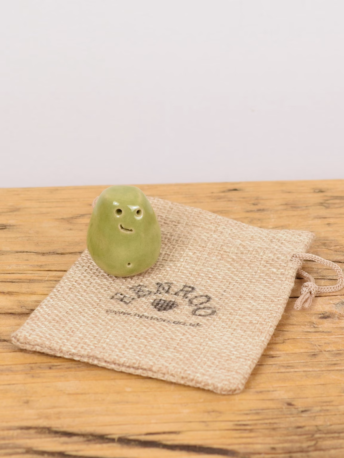 Mini Monster Moods single: one small green ceramic monster with a smiling face on a Henroo hessian gift bag