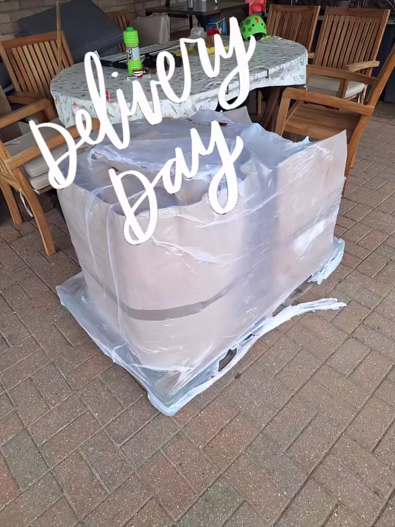 A kiln on a pallet, still wrapped in cardboard and plastic, on the patio